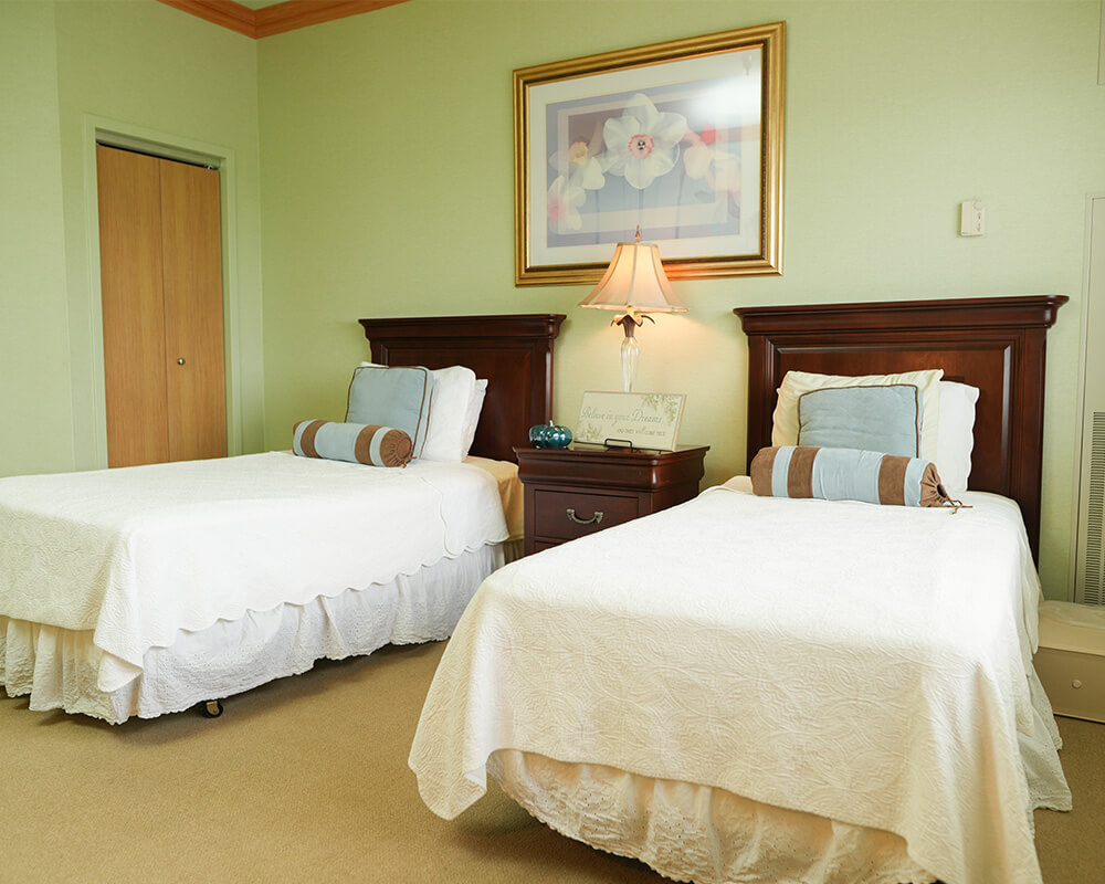 Two beds with white bedding in a cozy senior living unit with soft lighting.