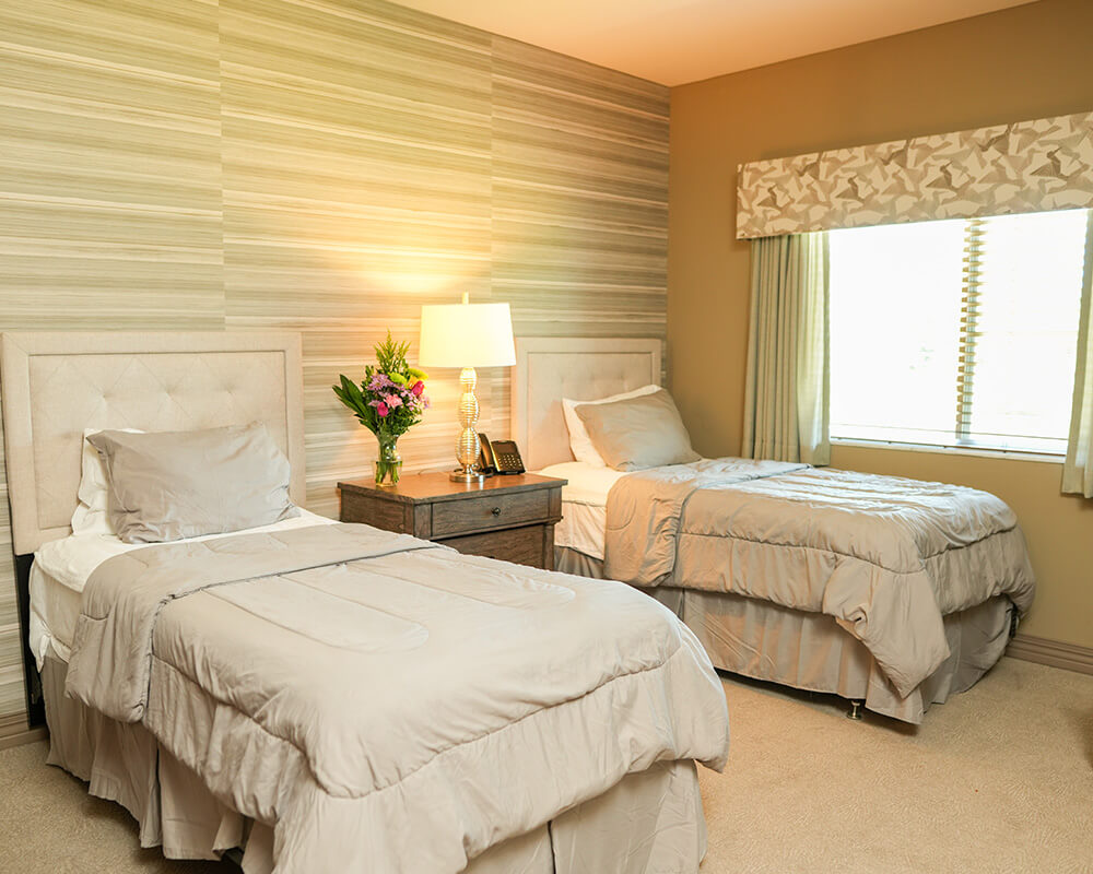 Cozy bedroom with twin four-poster beds and floral decor in a senior living unit.
