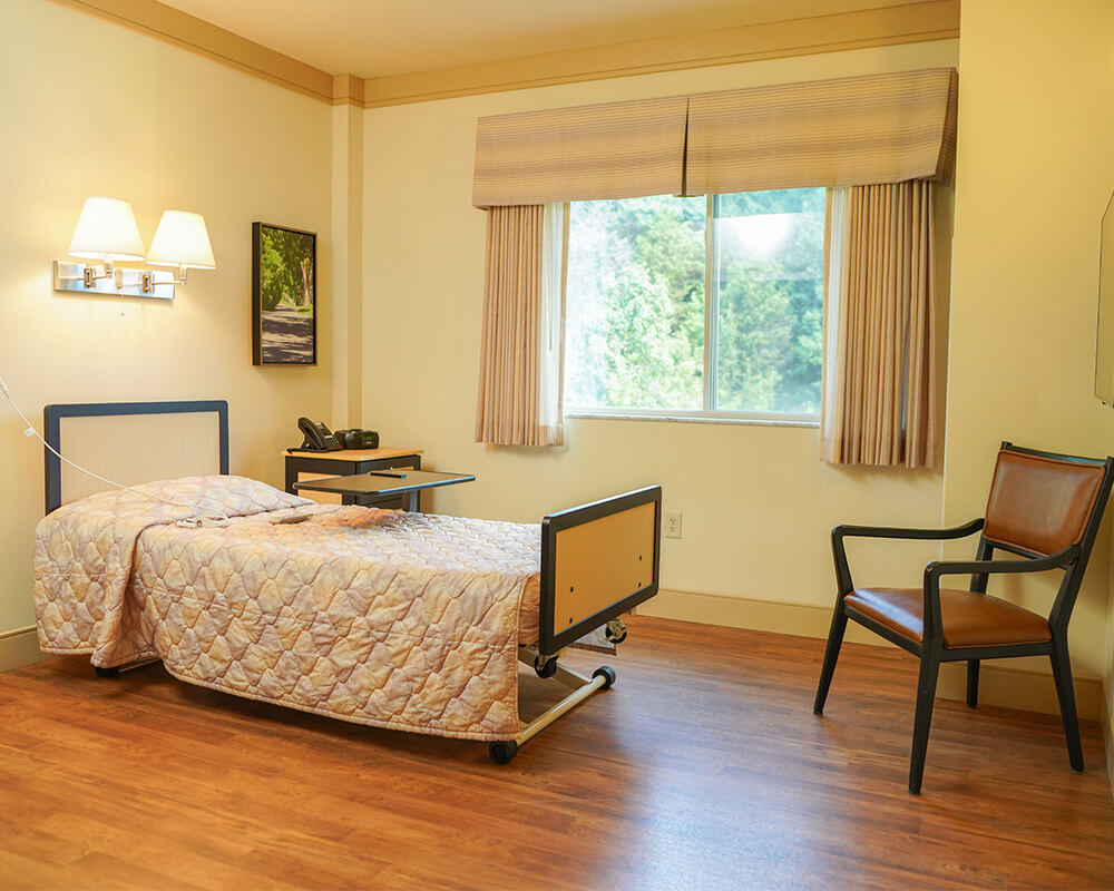 A cozy unit with a bed, chair, and window in a senior community.