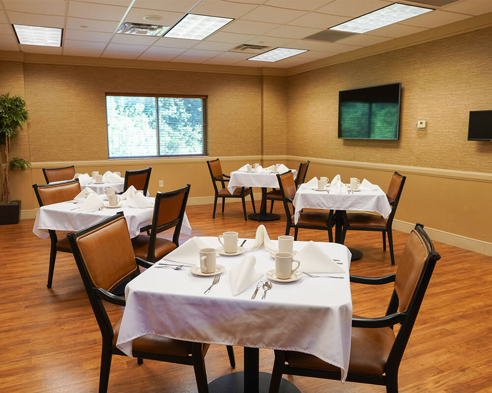 Dining area with neatly set tables and chairs in a senior living community.