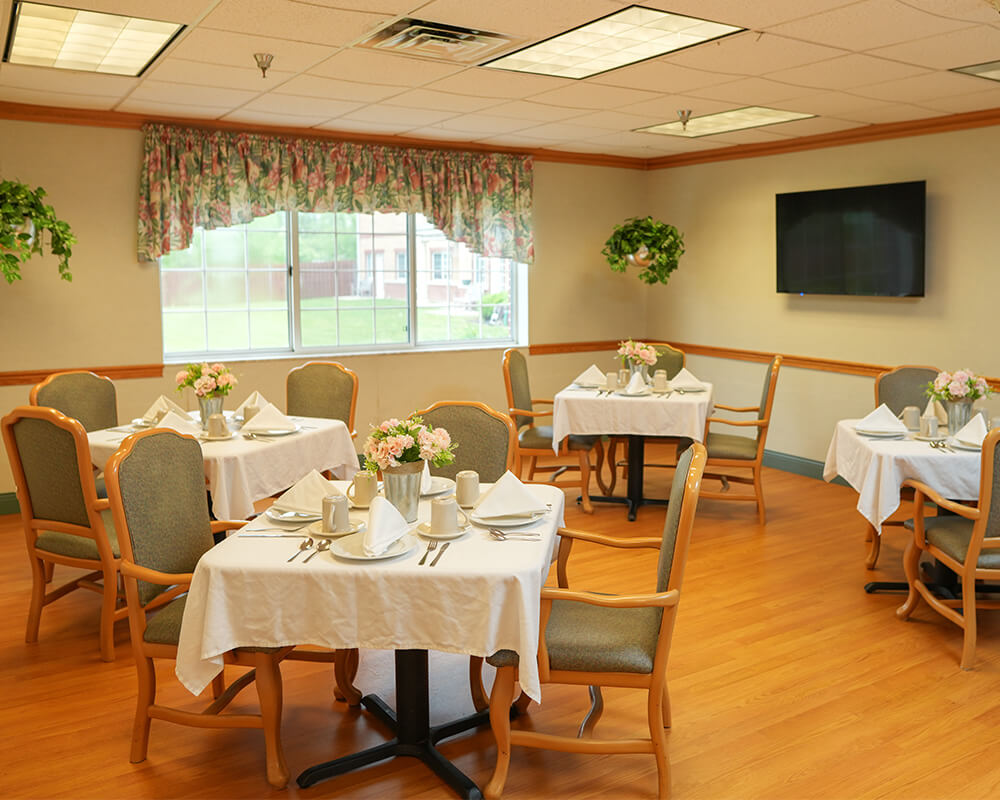 Dining area with tables set for meals in a senior living unit.