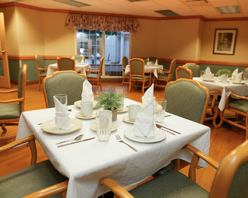 Elegant dining room with neatly set tables and green chairs in a senior living community.