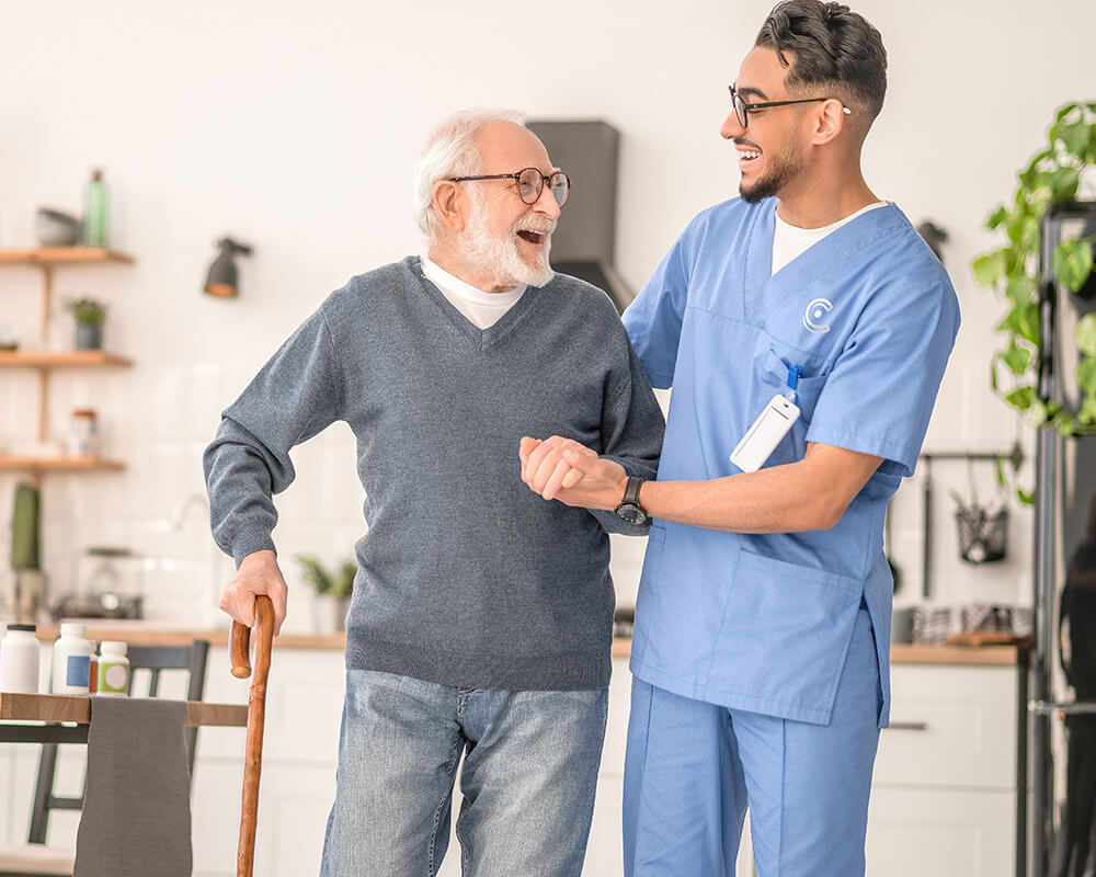 Smiling elder and caregiver walking in a bright, cozy living unit kitchen.