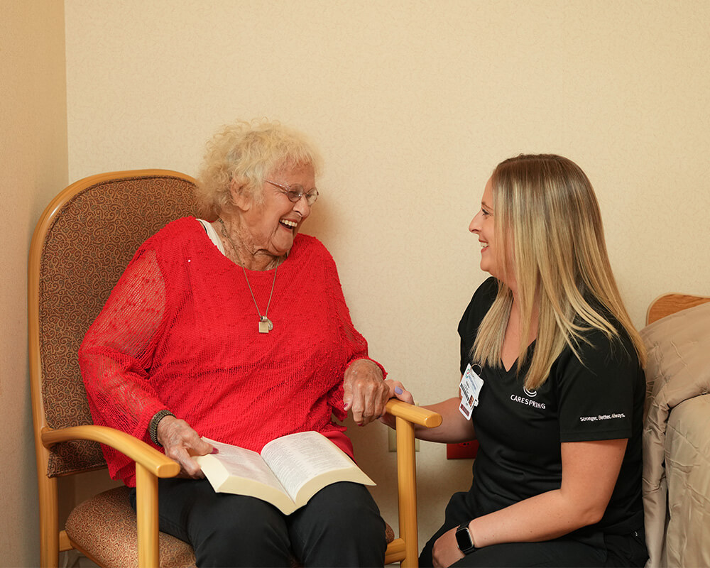 Elderly woman with caregiver sharing a laugh in a senior living unit.