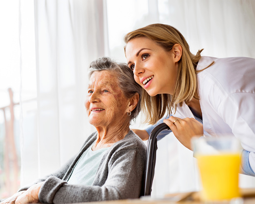 Young caregiver and elderly woman look out of a window