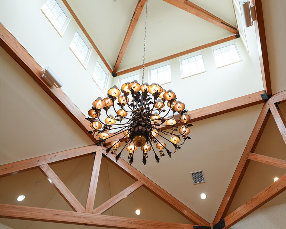 Large chandelier hanging from wooden beams in a bright atrium.
