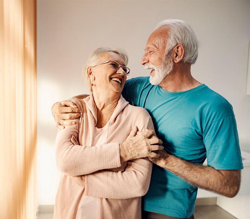 Senior man and woman embrace near a window in their home