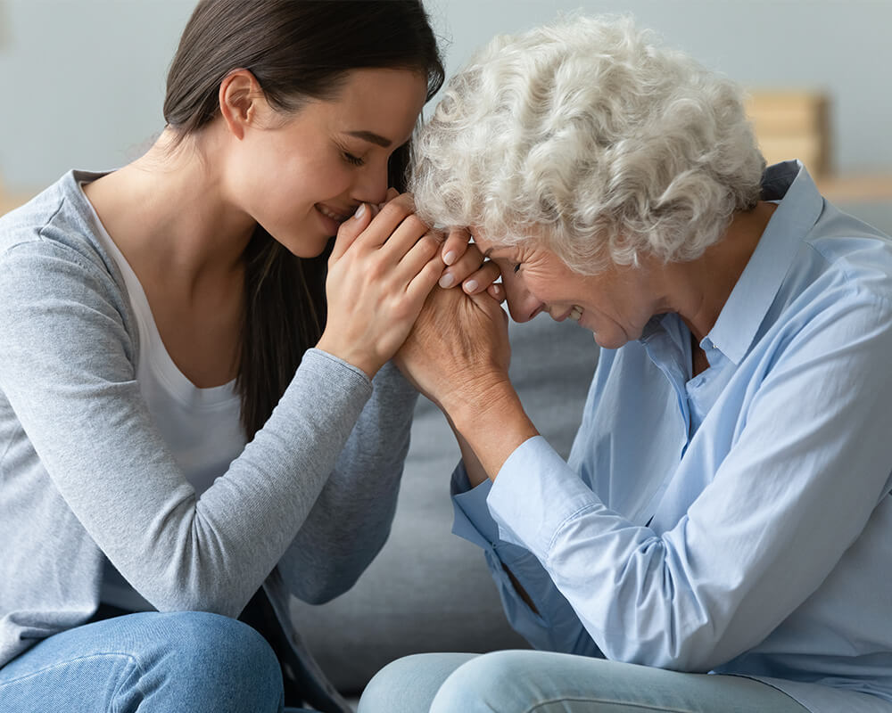 Two women share a heartfelt moment, holding hands and smiling warmly.