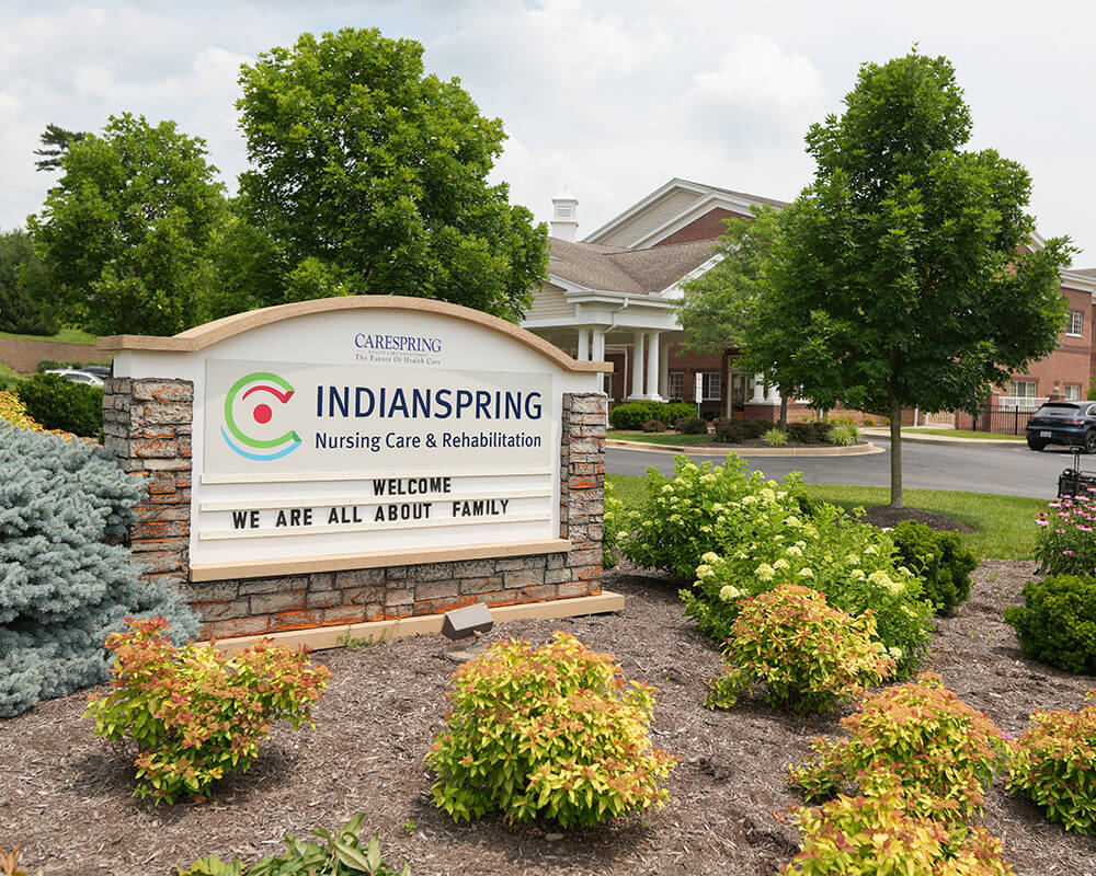 Entrance sign of Indianspring community surrounded by greenery and parking area.