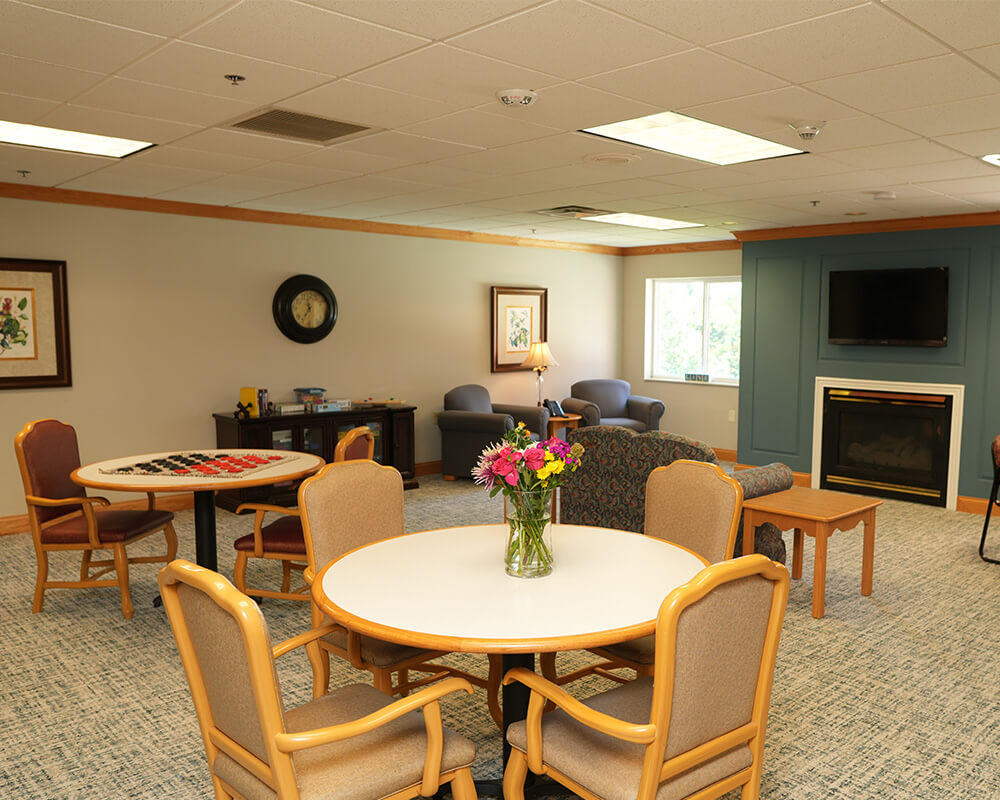 Cozy common area with tables, chairs, and a fireplace in a senior community unit.