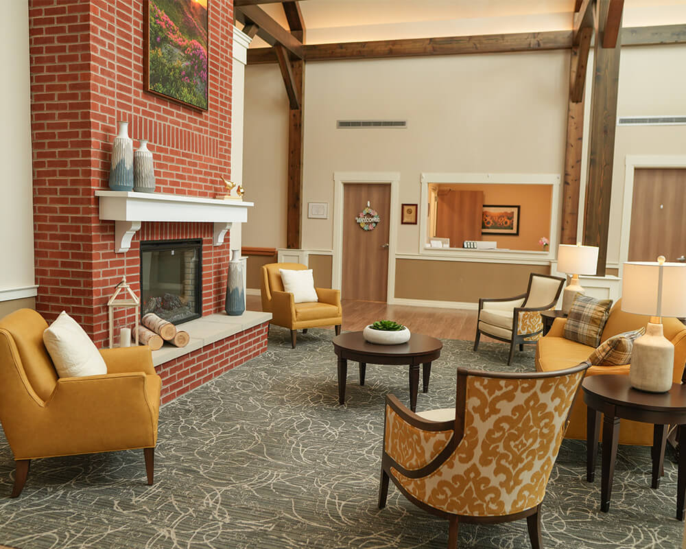 Cozy community room with seating and a brick fireplace in a senior living facility.