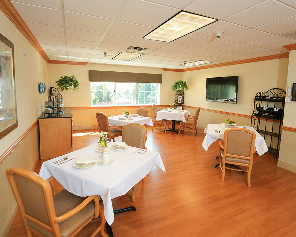 Dining area with set tables, chairs, TV, and bright window in a cozy unit.