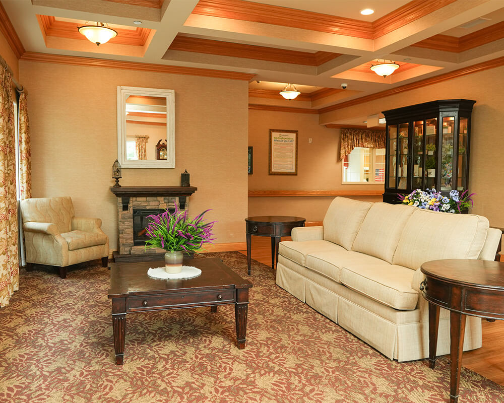 Warmly decorated lounge with sofa, armchair, and fireplace in a living community.