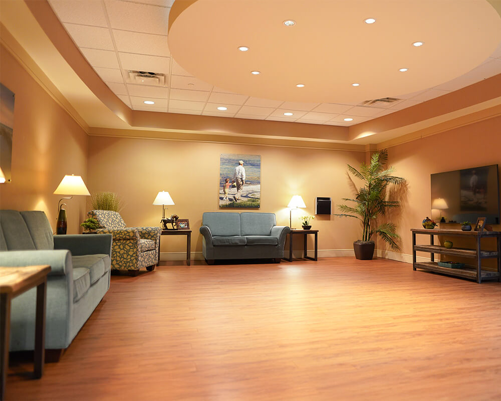 Cozy lounge area with seating, warm lighting, and a wall painting in a senior living community.