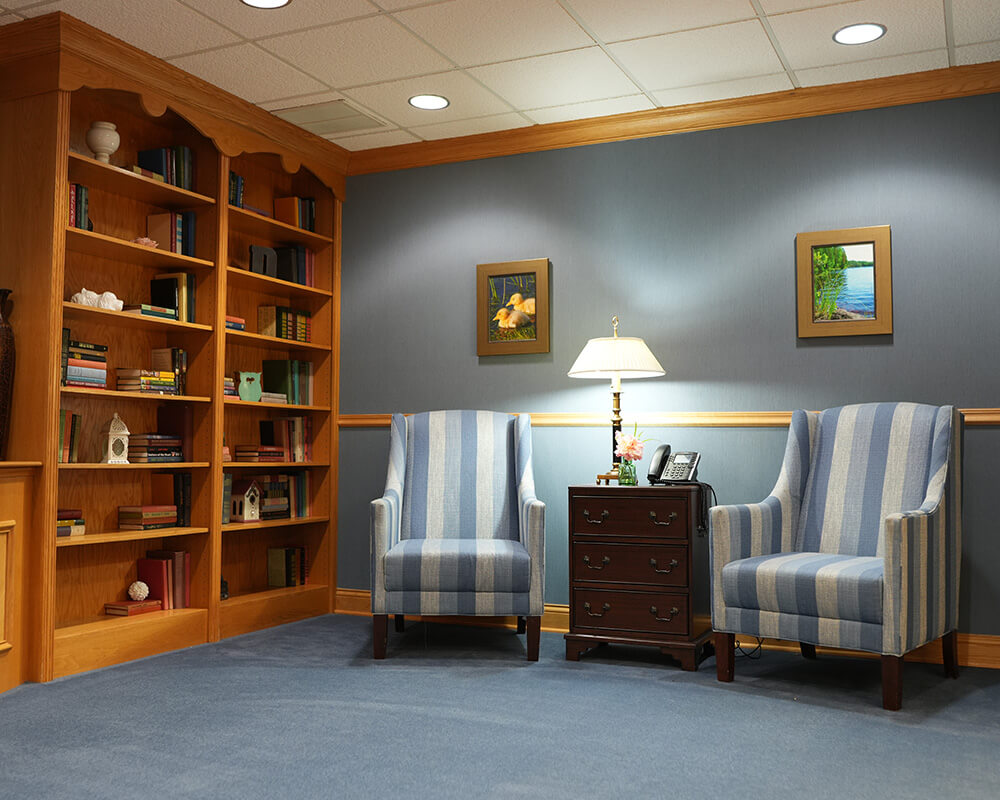 Cozy seating area with striped chairs, a lamp, and a wooden bookshelf in a living unit.