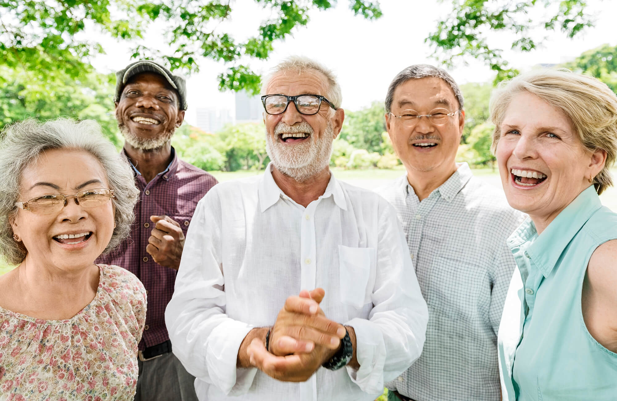 A diverse group of five smiling seniors enjoying a sunny day outdoors.