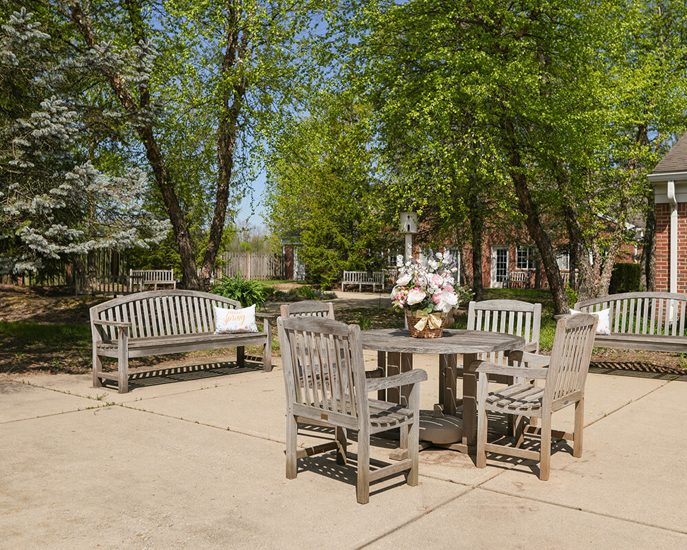 Outdoor patio with wooden tables and benches, surrounded by lush green trees.