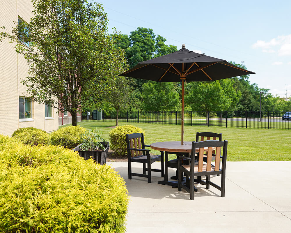 Outdoor patio with table, chairs, and umbrella near landscaped garden at senior living.