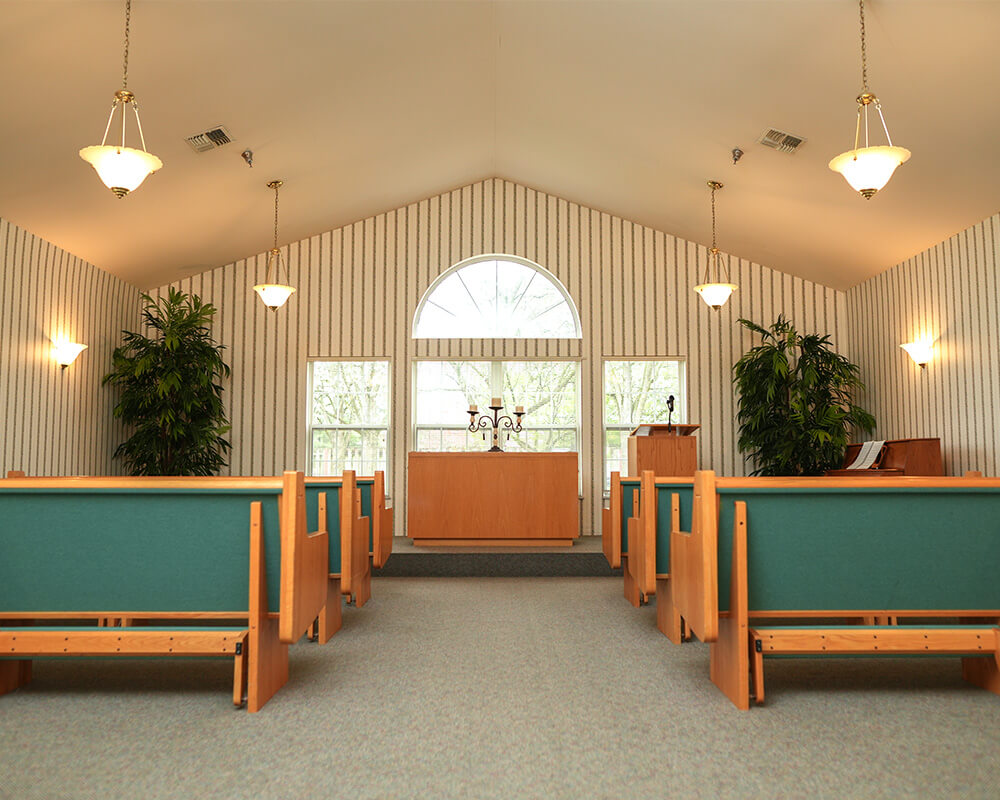 Chapel with rows of wooden benches and large arched window in a senior community.