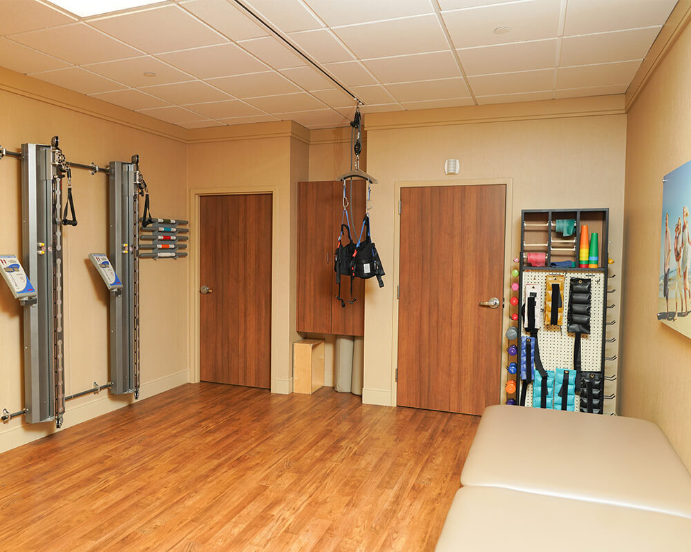 Rehabilitation room with exercise equipment and wooden flooring.