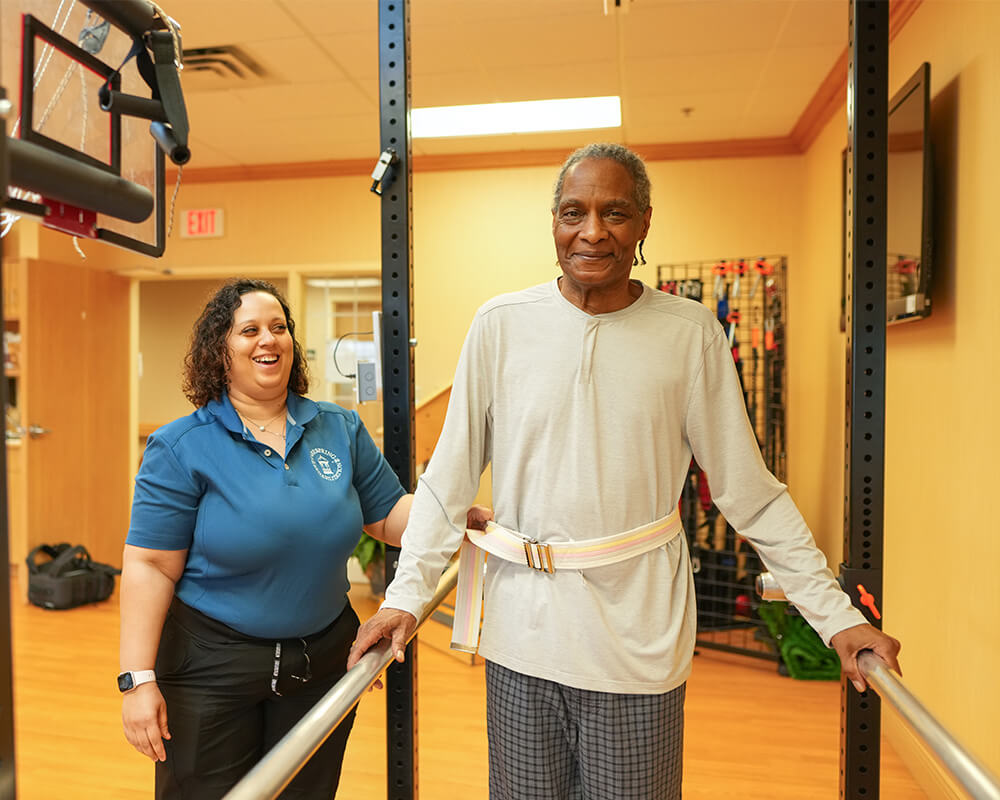 Elderly man with therapist walking in rehabilitation area at senior community.
