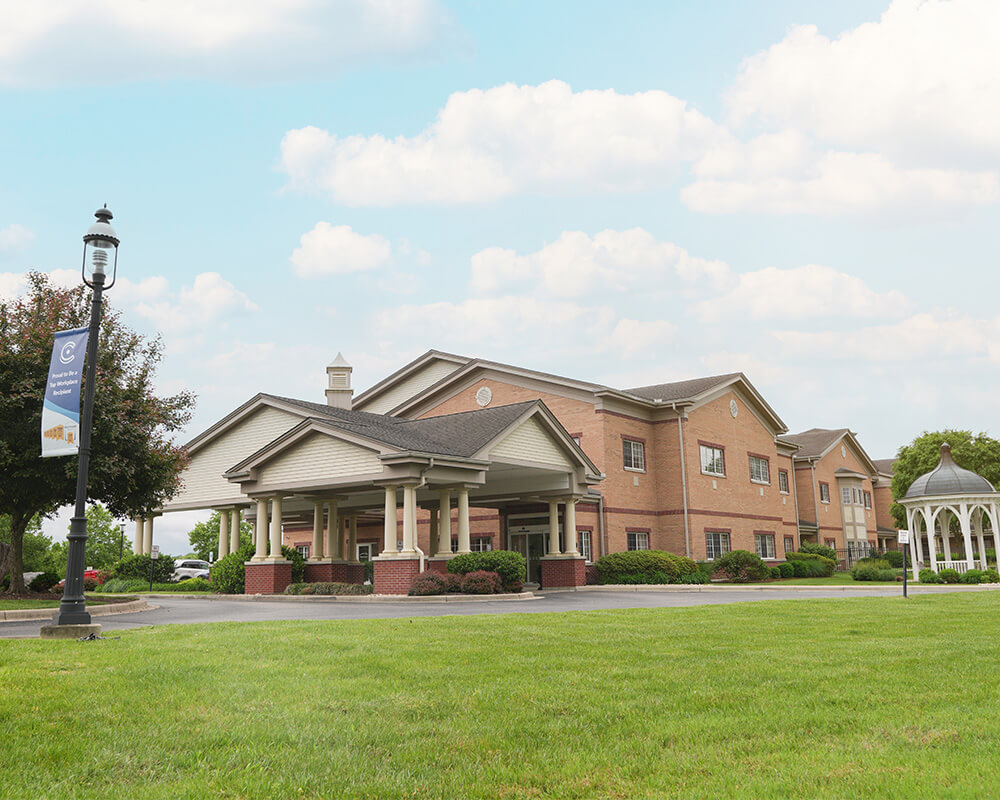 Brick building with a gabled roof and gazebo, surrounded by a green lawn.