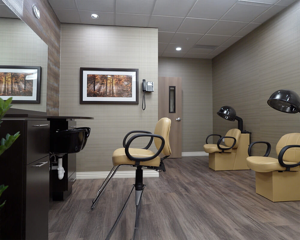 Hair salon with beige chairs and framed art in senior living community.