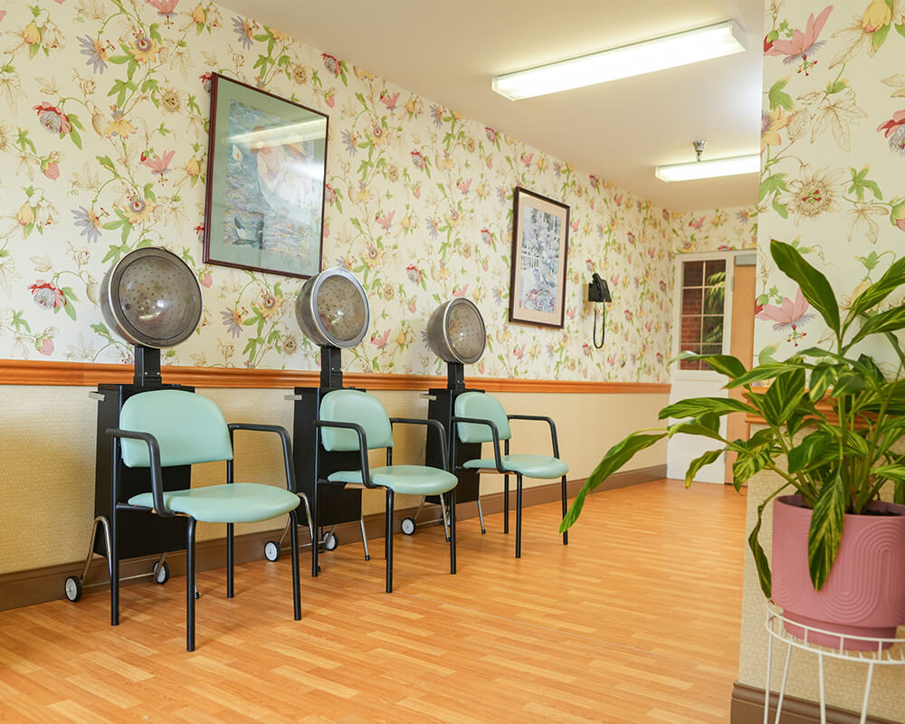 Salon area in senior living community with three hair dryers and floral wallpaper.