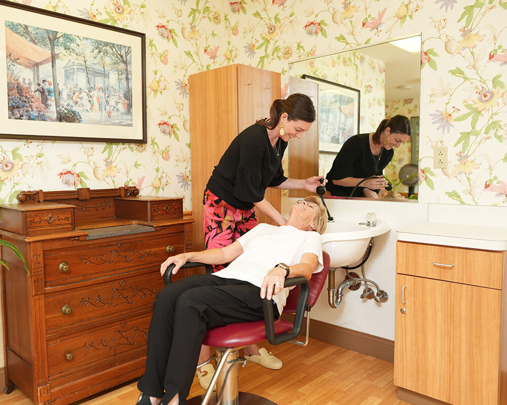 Woman assists another woman at a salon inside a senior community.