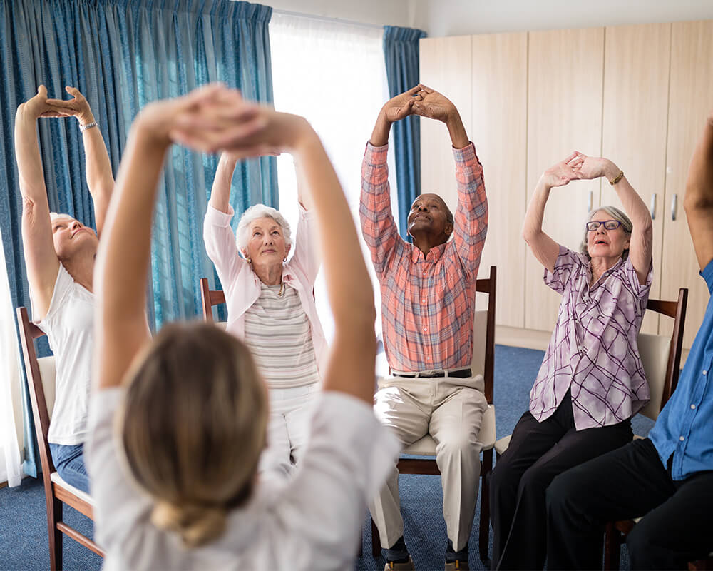 Group of seniors participating in a seated exercise in a bright room.