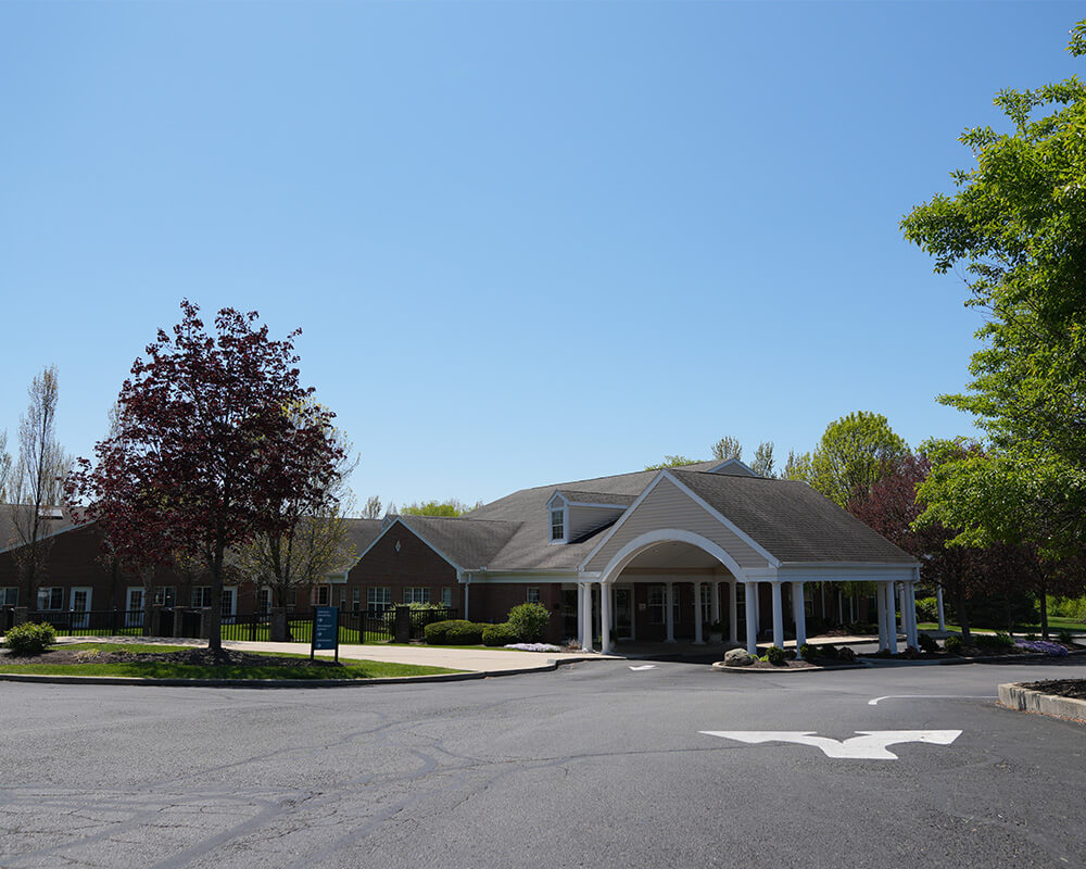 Main building of a senior living community with a large entrance and surrounding trees.
