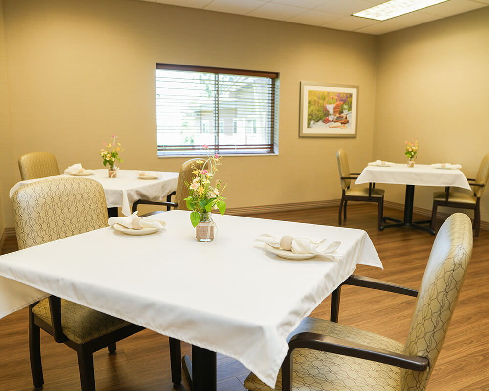 Spacious dining area in a comfortable community setting with round tables and chairs.