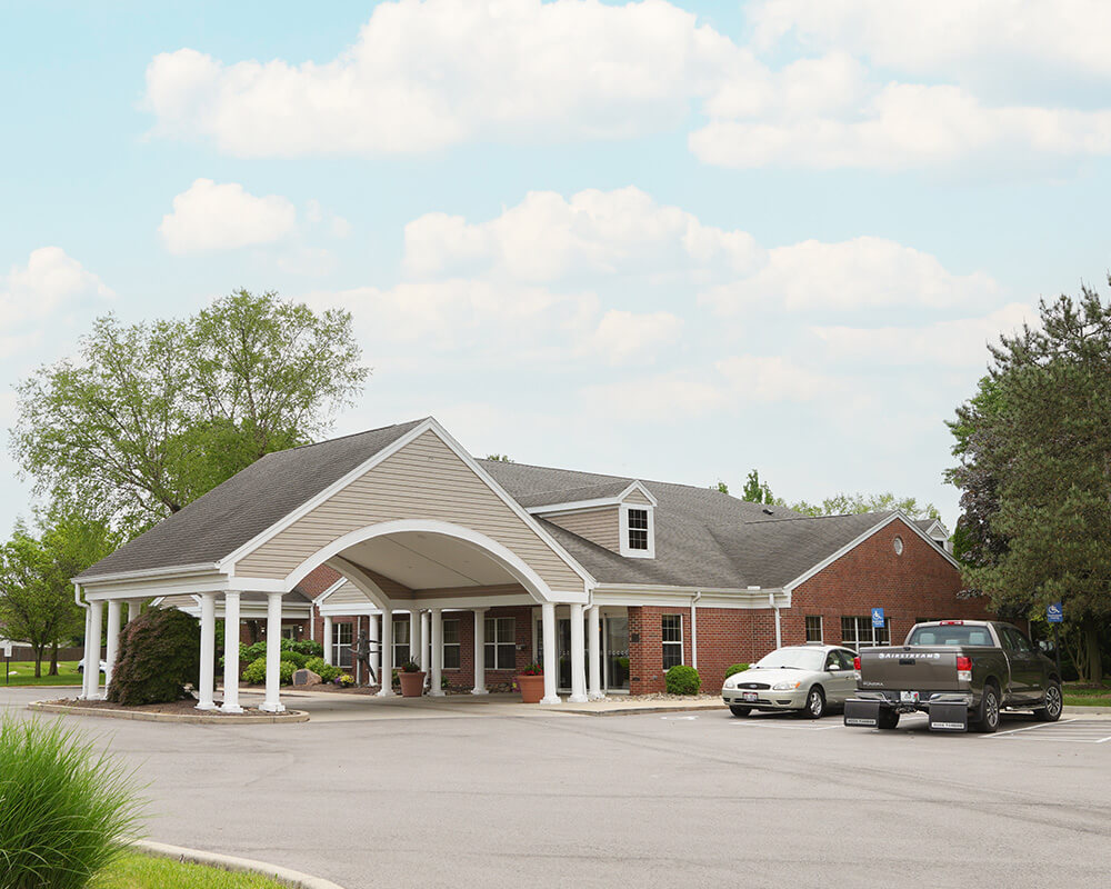 Senior living community entrance with parking area and landscaped surroundings.