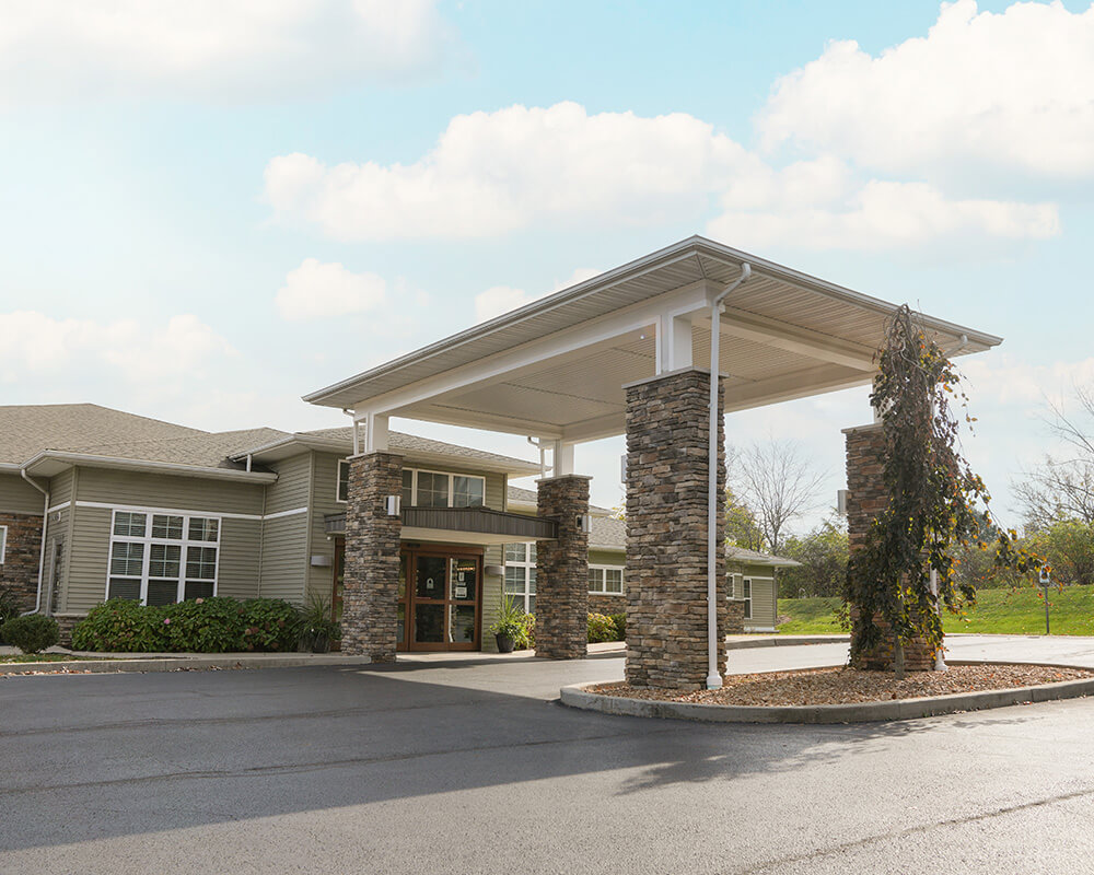 Entrance of a senior living community with green awning and brick facade.