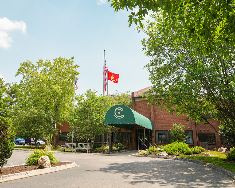 Entrance of a senior living community with green awning and brick facade.