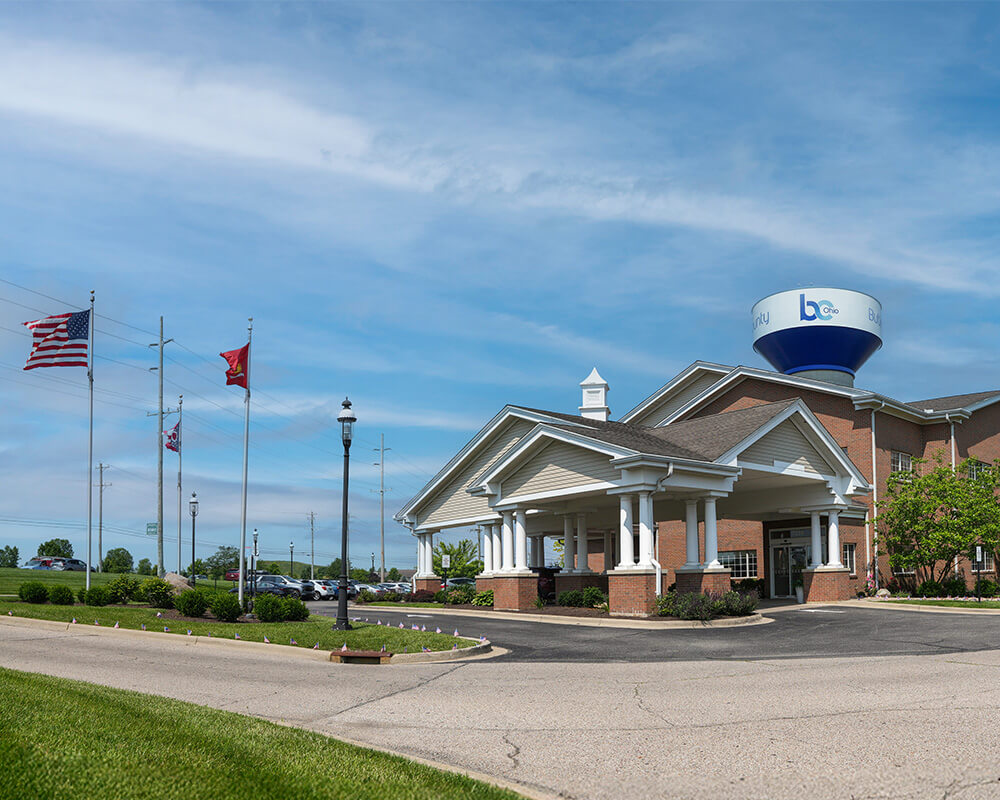 Entrance of a senior living community with flags and a water tower in the background.