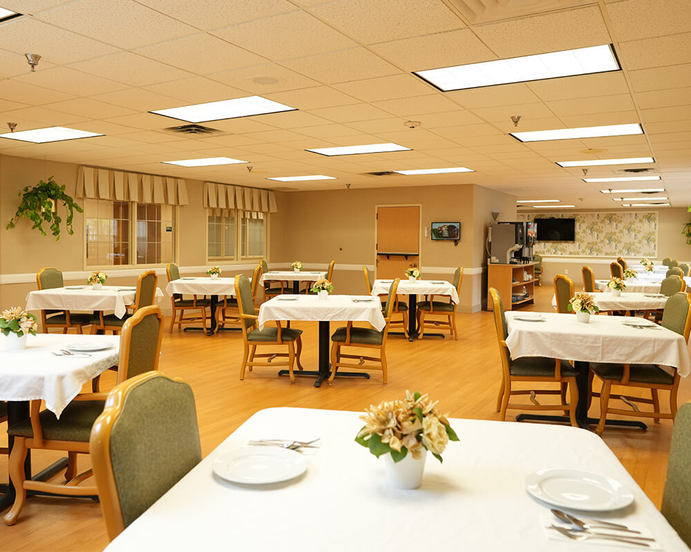 Bright dining area with four tables in a senior living unit.