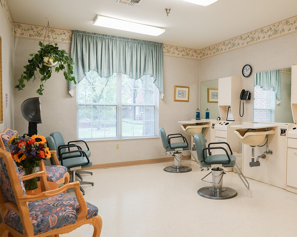 Bright salon area with two styling chairs and a bouquet in a senior living unit.