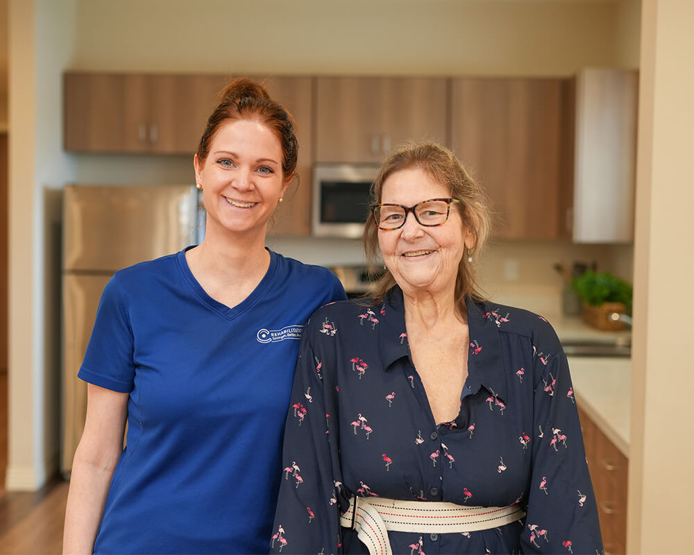 Smiling staff member with resident in senior living kitchen environment.
