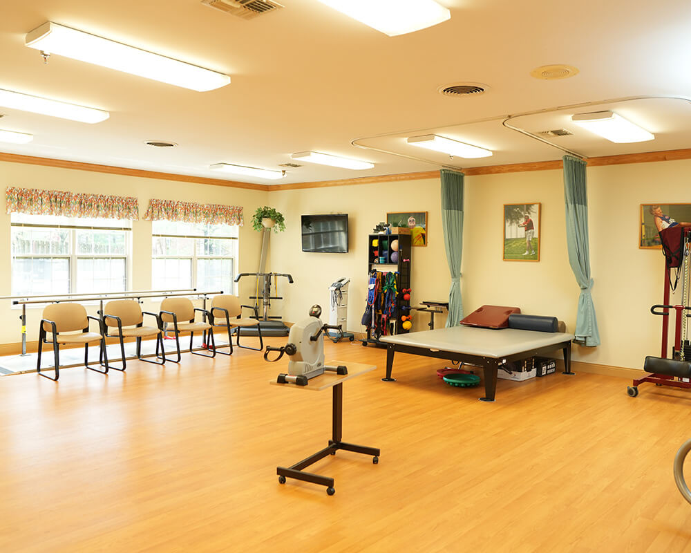 Spacious therapy room with exercise equipment and chairs in a senior living community.