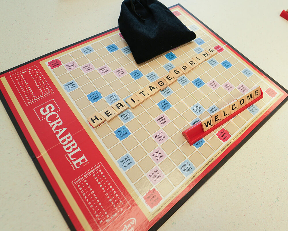 Scrabble board spelling HERITAGE SPRING and WELCOME with a tile bag.