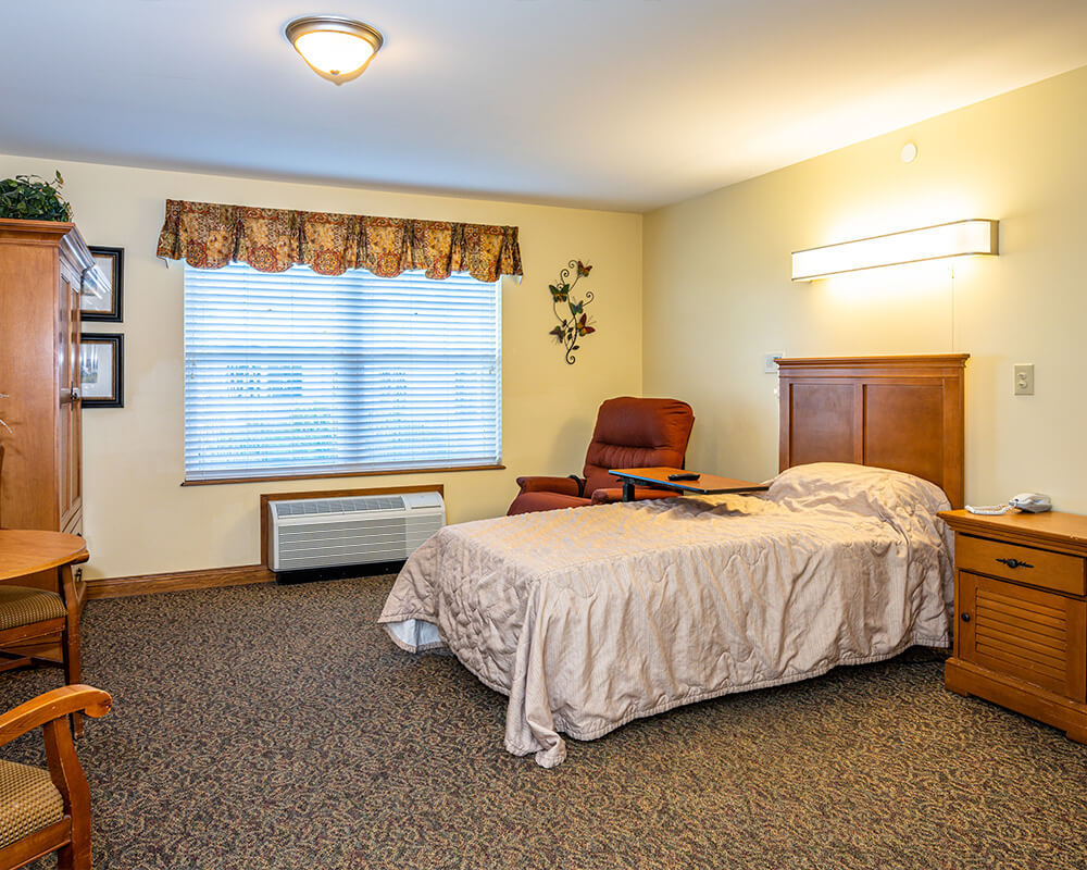 Cozy living unit with bed, armchair, and window with floral curtain.