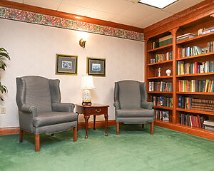 Cozy reading corner with armchairs, a lamp, and a bookshelf in a senior community.