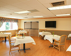 Dining room with tables set for meals in a senior living community center.