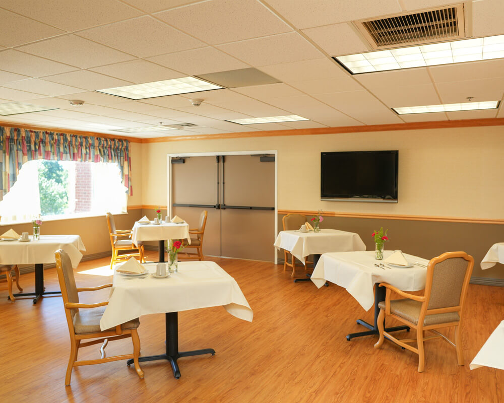 Dining room with tables set for meals in a senior living community center.