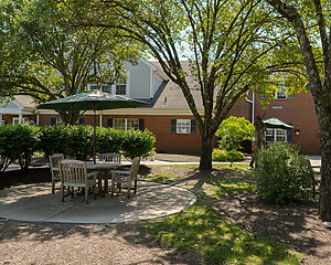 Outdoor seating area with umbrella near brick building under tree shade.