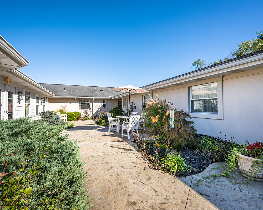 Outdoor patio with seating and umbrella surrounded by landscaped gardens in residential community.