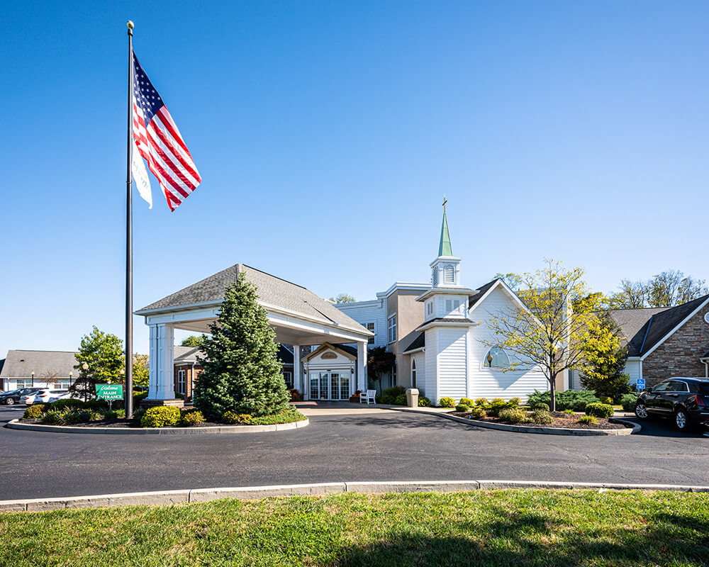 Front view of a senior living community with American flag and well-kept landscape.
