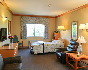 Cozy senior living unit with bed, recliner, and window view.