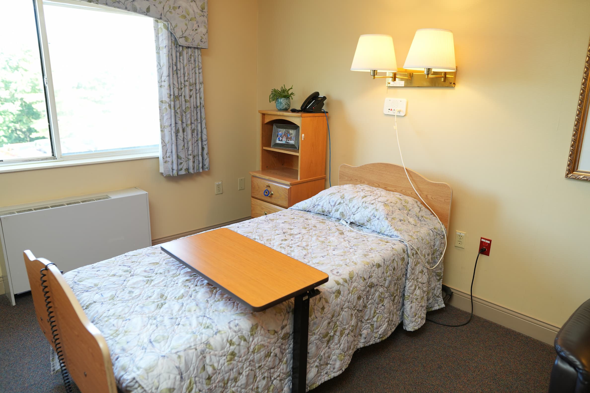 Cozy senior living unit with bed, wooden furniture, and large window.